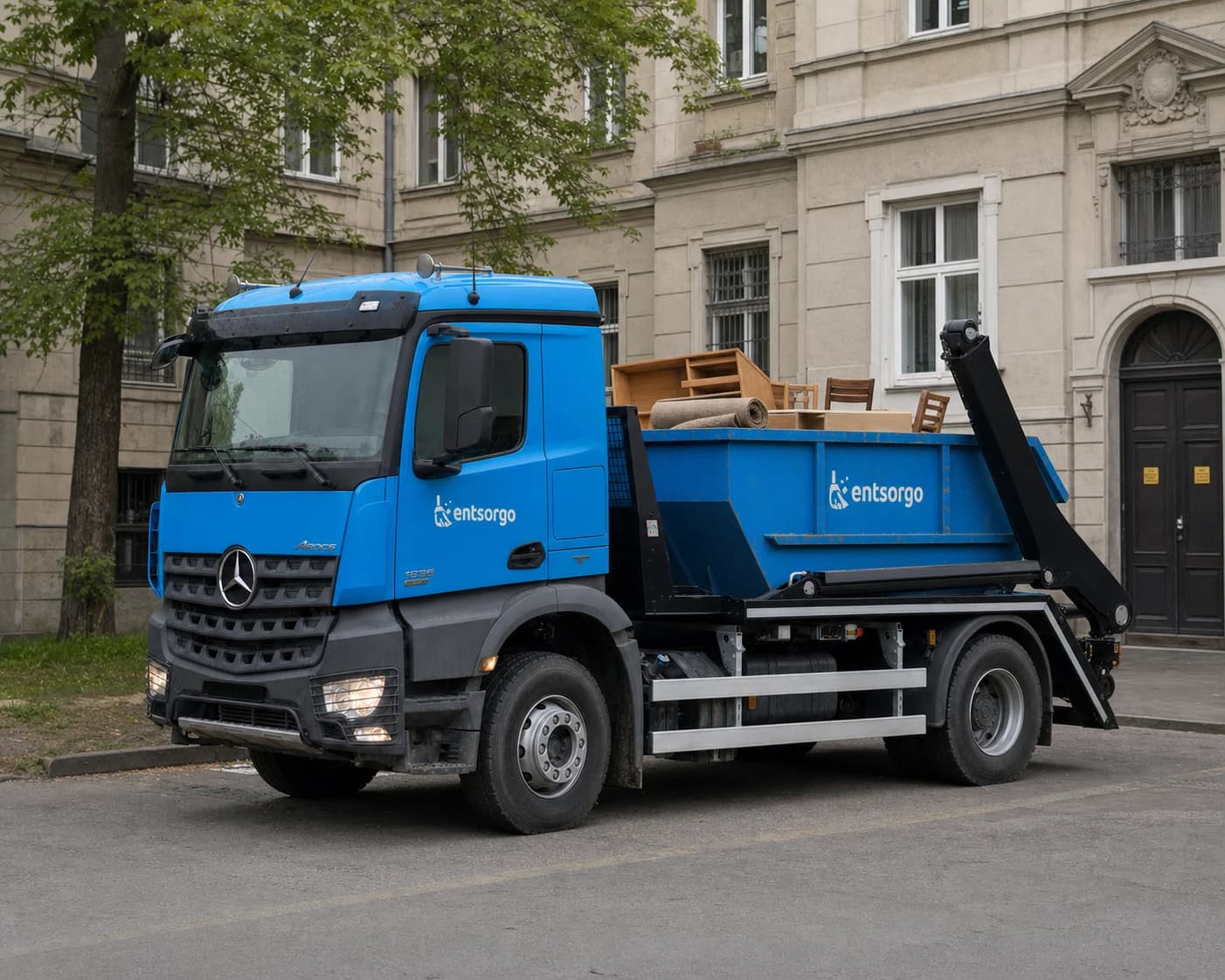 Entsorgo konténerszállító teherautó bútorokkal egy budapesti épület előtt